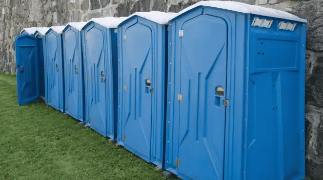 Row of blue portable toilets lined up on grass against a stone wall for event sanitation in Richmond, VA