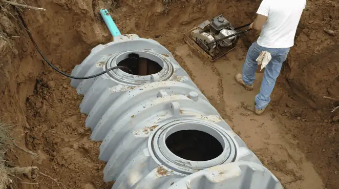 Septic tank installation showing a technician compacting soil around a new poly septic tank in an excavation pit in Richmond, VA